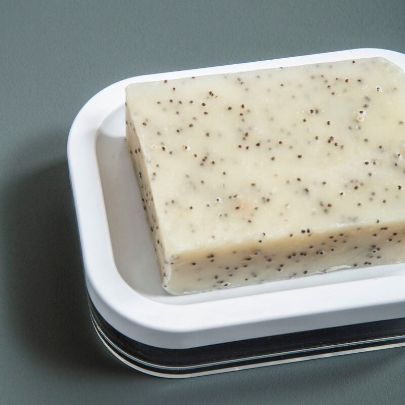 Bar of soap with specks on a white soap dish against a gray background