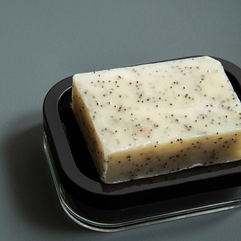 Bar of soap with specks on a black tray against a gray background