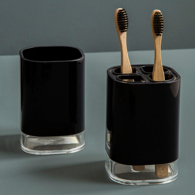 Black glass toothbrush holder with wooden toothbrushes on a gray background