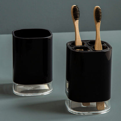 Black glass toothbrush holder with wooden toothbrushes on a gray background