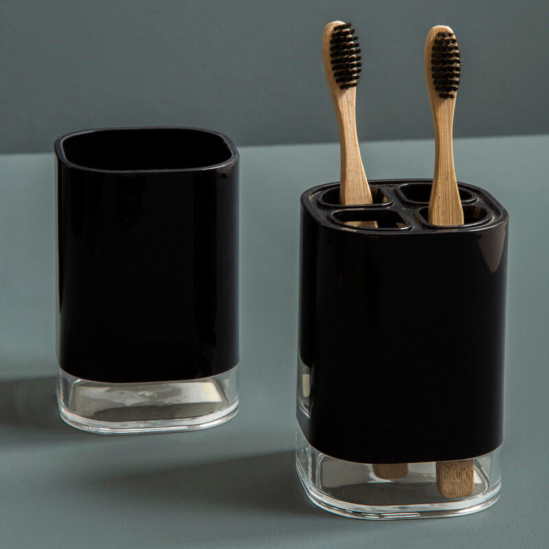 Black glass toothbrush holder with wooden toothbrushes on a gray background