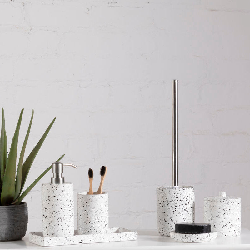 Bathroom accessories including a plant, soap dispenser, toothbrush holder, and toilet brush holder on a white surface with a light gray wall background.