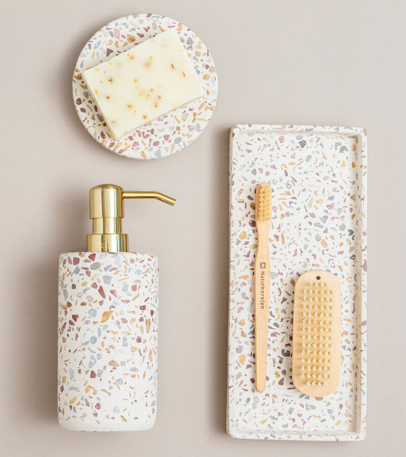 Bathroom set with terrazzo-patterned dispenser, soap, toothbrush, and scrubber on a beige background