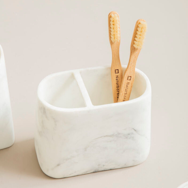 White marble toothbrush holder with two bamboo toothbrushes on a light background