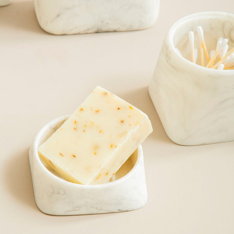 Bar of soap in a white ceramic dish on a light beige surface