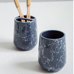 Two blue marbled ceramic cups with wooden toothbrushes on a light gray background