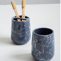 Two blue marbled ceramic cups with wooden toothbrushes on a light gray background