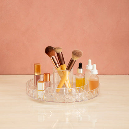 Makeup brushes and bottles on a clear acrylic tray against a pink background