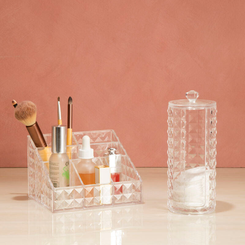 Clear acrylic organizer with cosmetic items on a light surface against a pink wall