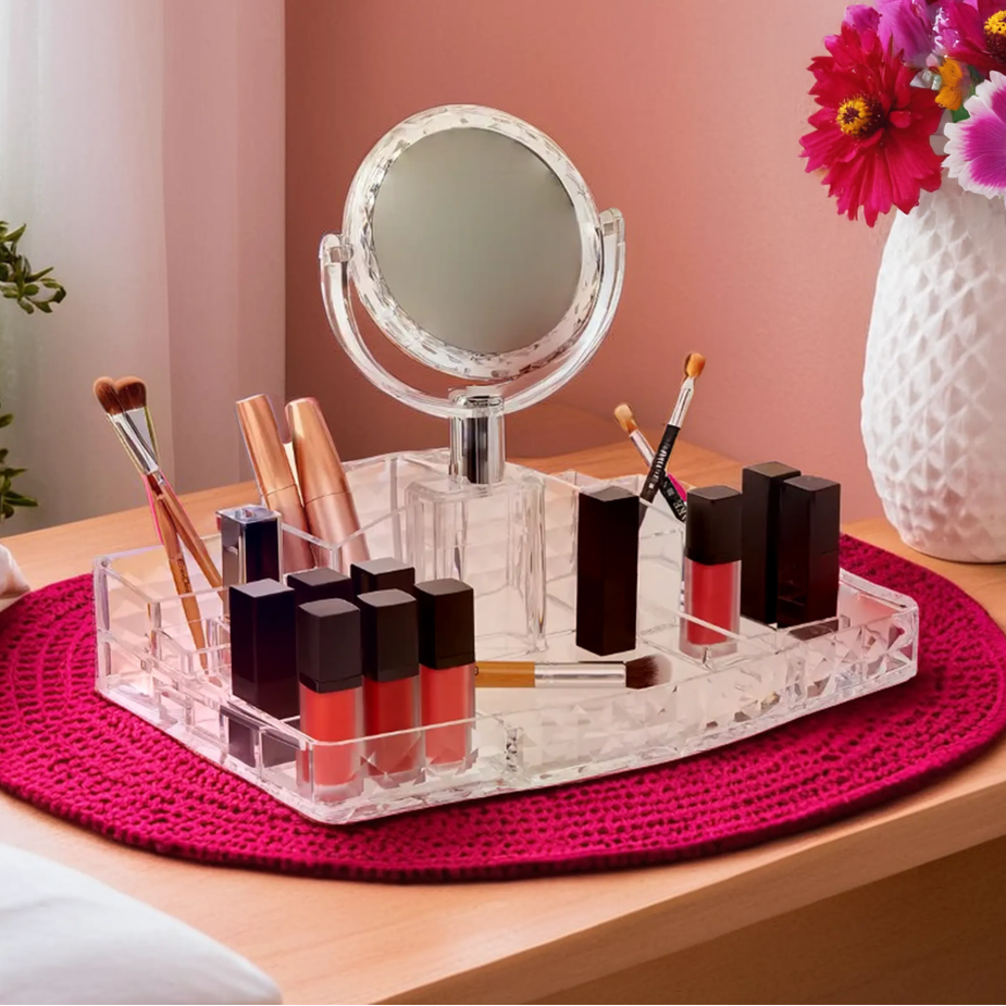 Makeup station with mirror, bottles, and brushes on a pink mat with a vase of flowers in the background.