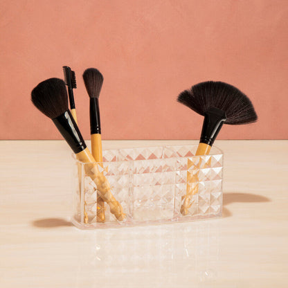 Set of makeup brushes in a clear holder against a pink background