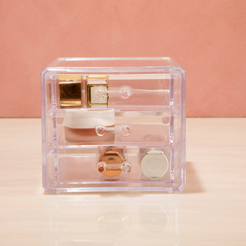 Clear jewelry box with gold and rose gold jewelry on a pink background