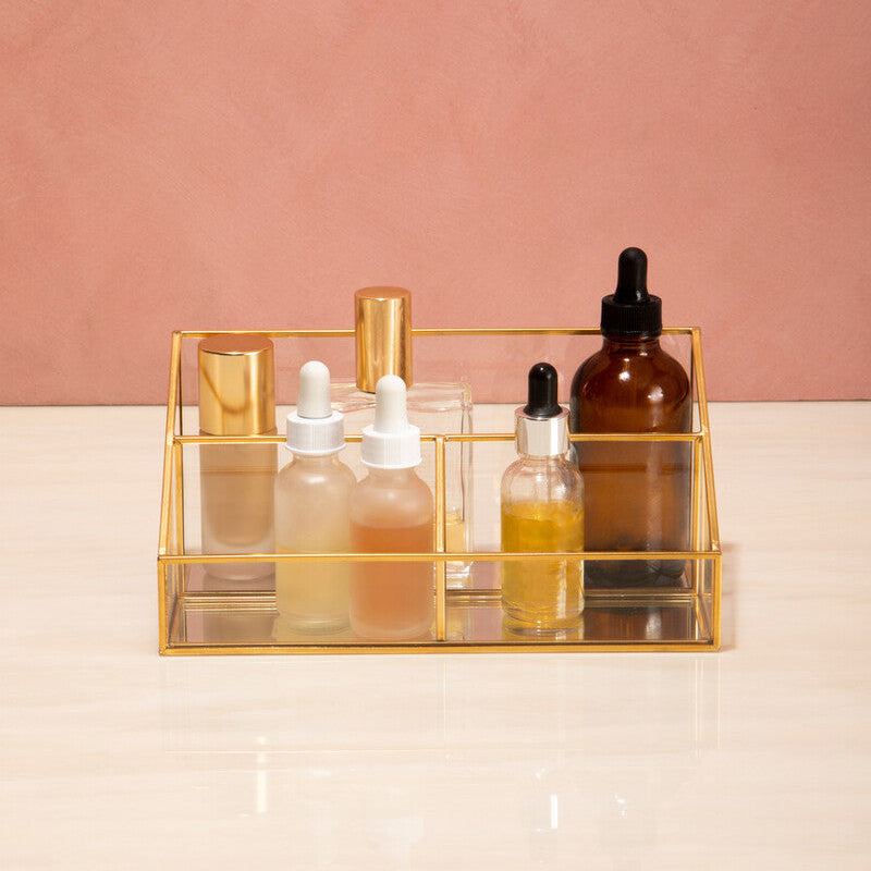Set of skincare bottles with droppers on a gold tray against a pink background
