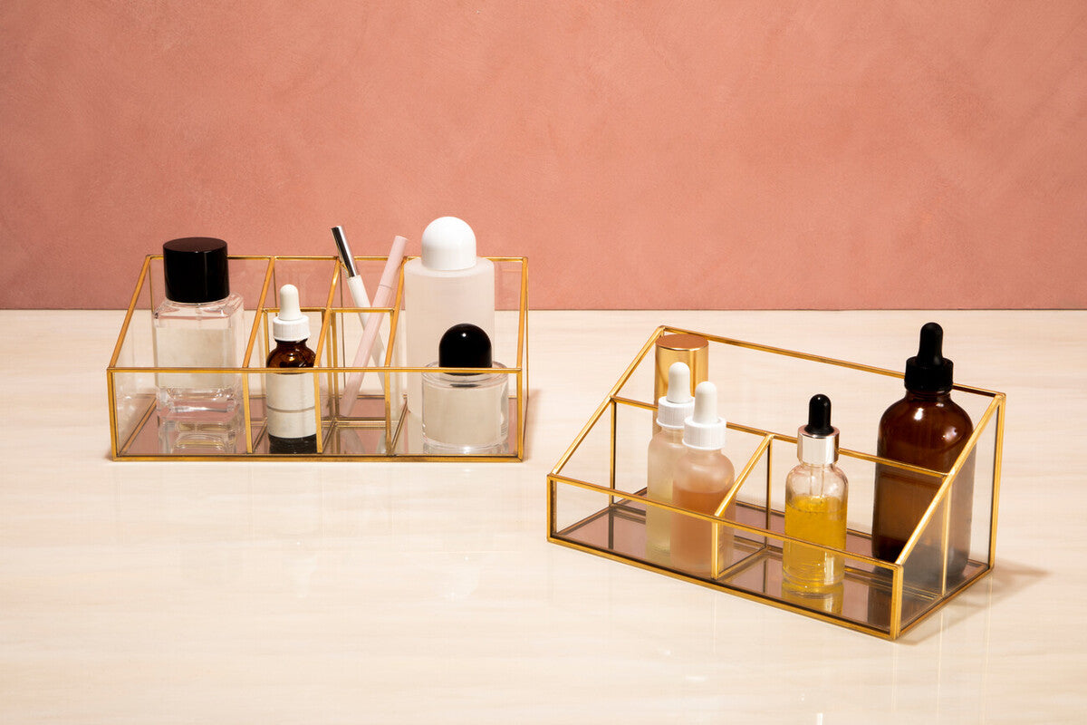 Two gold rectangular trays with skincare products on a pink background