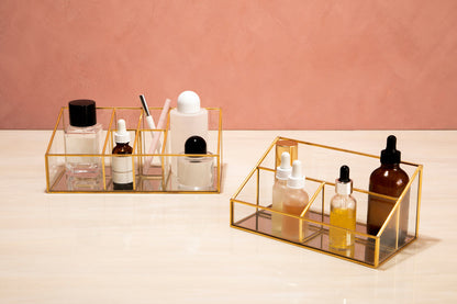 Two gold rectangular trays with skincare products on a pink background