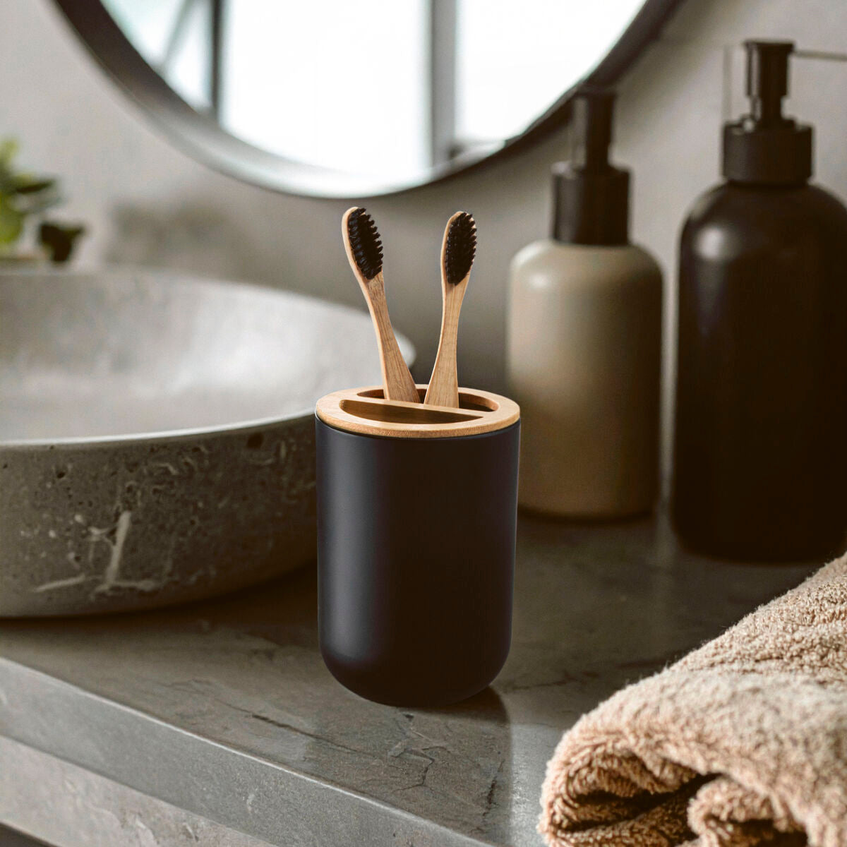 Bathroom setting with a black toothbrush holder containing wooden toothbrushes, a towel, and various bottles.