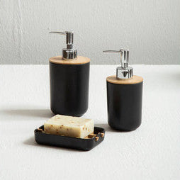 Two black soap dispensers with wooden accents on a white surface against a gray wall.
