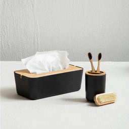 Black tissue box and holder with tissues, toothbrushes, and a soap bar on a white surface.