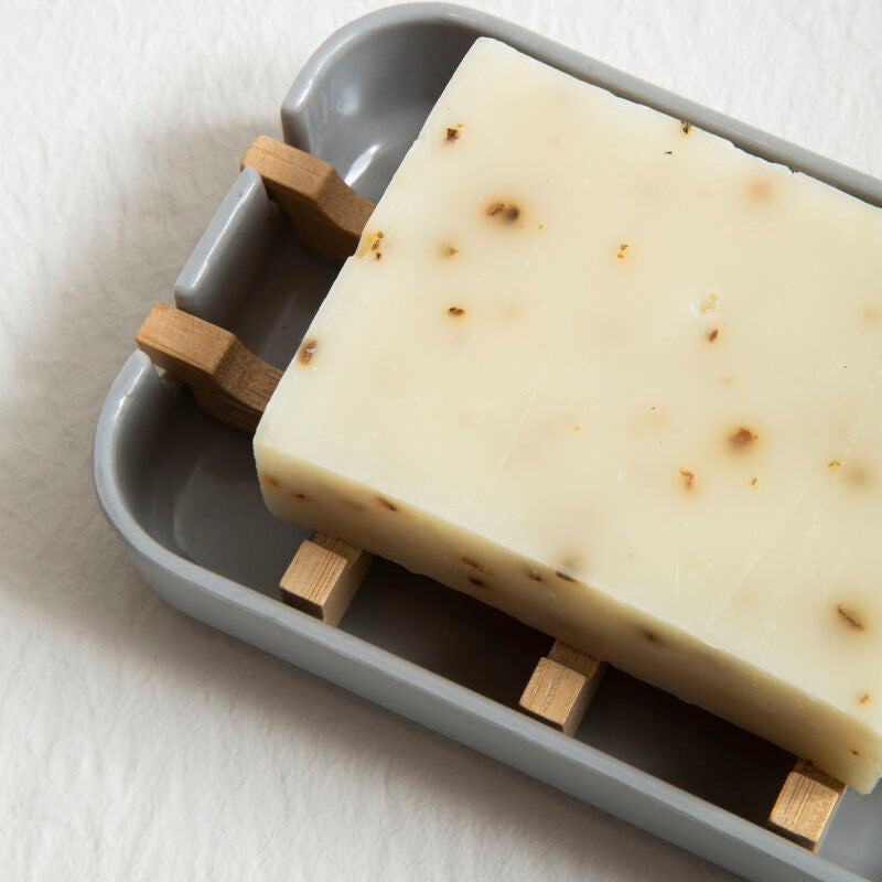 Bar of soap with wooden exfoliation pads on a gray soap dish against a white background
