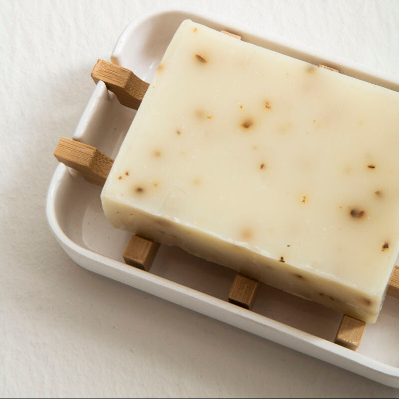 Bar of soap on a white tray with wooden stands against a light background