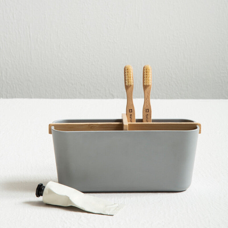Gray container with bamboo toothbrushes and a white cloth on a light gray background