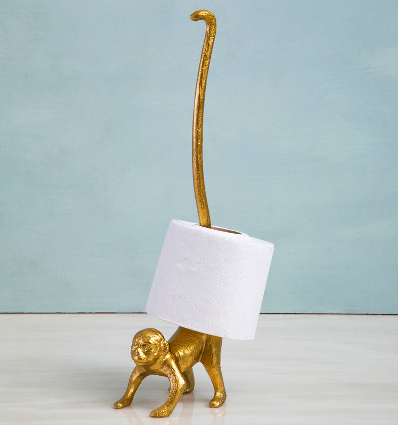 Gold monkey-shaped toilet paper holder with a roll of toilet paper on a light blue background