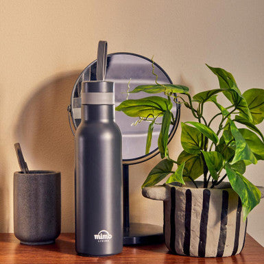 Gray water bottle with straw on a wooden surface next to a plant and small container.