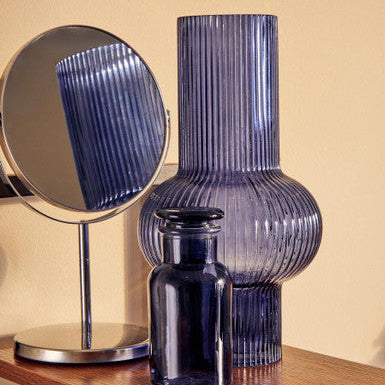 Blue ribbed vase on a wooden surface with a mirror reflecting the vase.