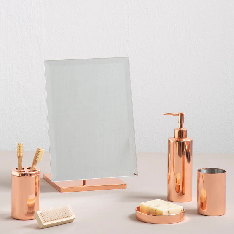 Bathroom accessories including a mirror, soap dispenser, and cups on a light surface.