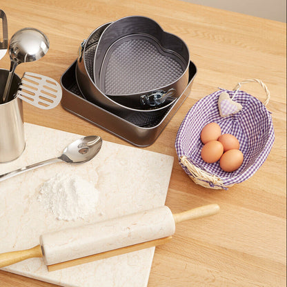Kitchen utensils and tools on a wooden surface including a rolling pin, spatulas, and a basket of eggs.