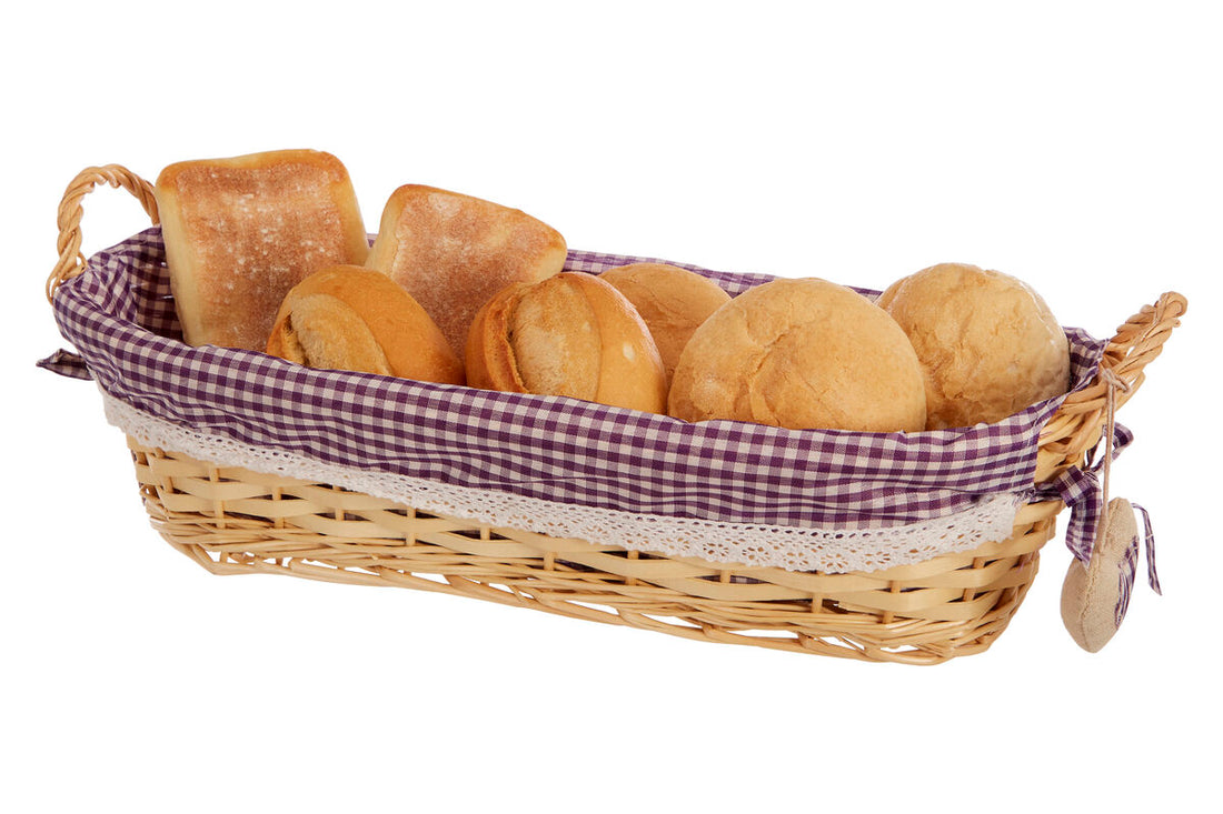 Wicker bread basket with checkered liner containing bread rolls on a white background