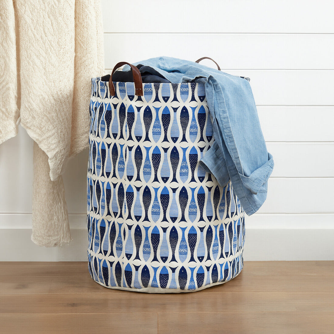 Patterned laundry basket with clothes on a wooden floor against a white wall