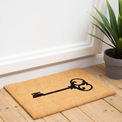 Doormat with a key design on a wooden floor next to a plant