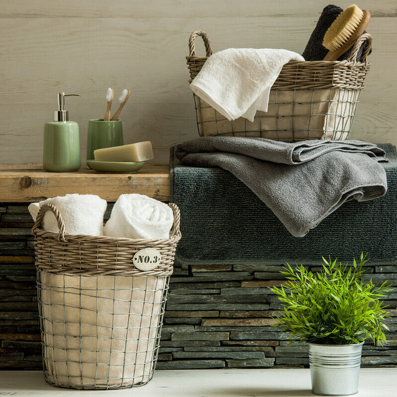 Wicker baskets with towels and a plant on a wooden floor against a wooden wall.