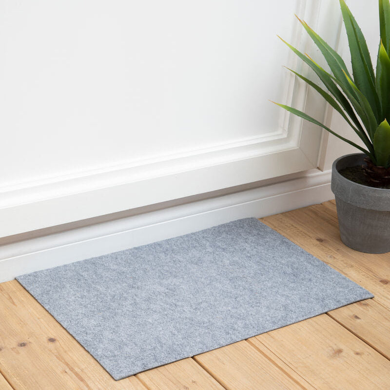 Gray doormat on a wooden floor with a plant in the corner