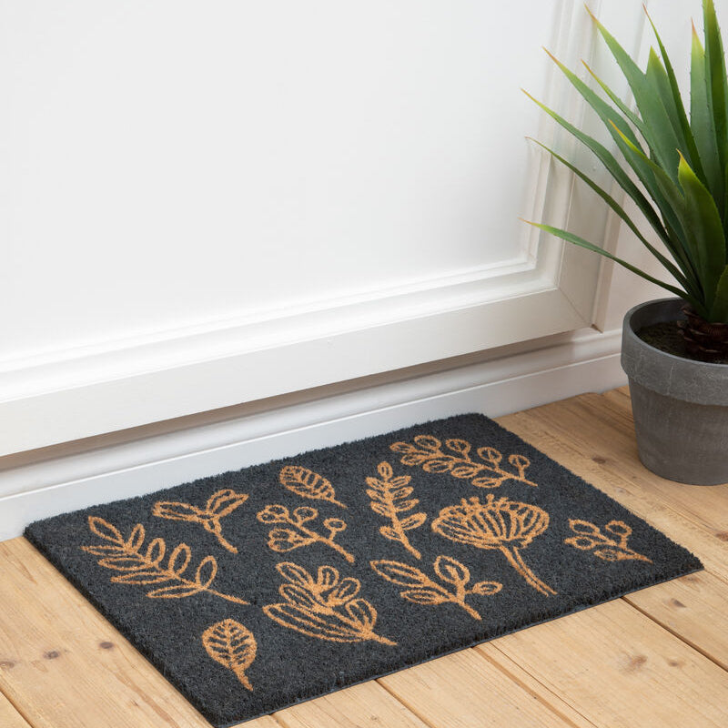 Decorative doormat with floral patterns on a wooden floor next to a plant.