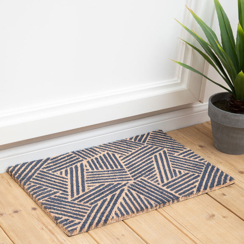 Doormat with geometric pattern on a wooden floor next to a plant