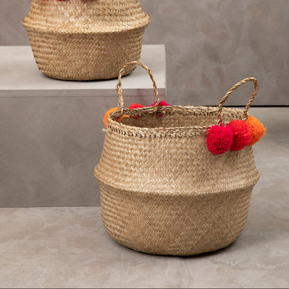 Two woven baskets with pom-pom handles on a gray surface and background.