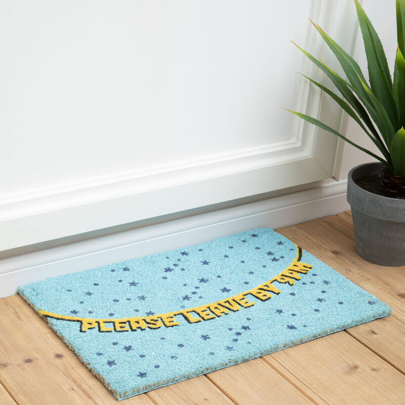 Light blue doormat with yellow text on a wooden floor next to a plant.