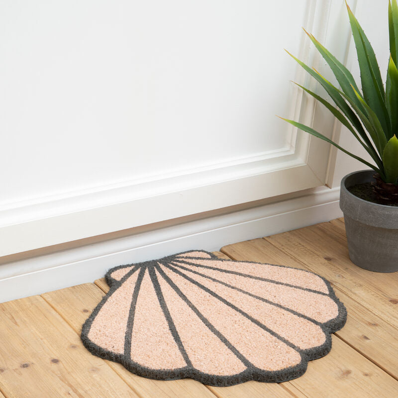 Shell-shaped doormat on a wooden floor with a plant in the background