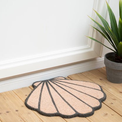 Shell-shaped doormat on a wooden floor with a plant in the background