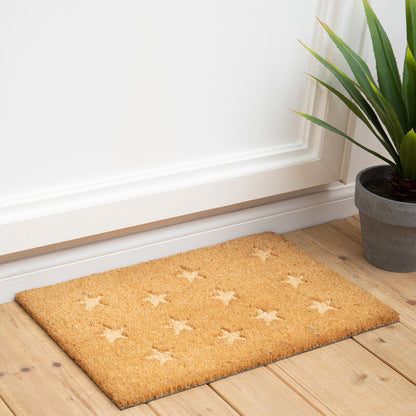 Doormat with star patterns on a wooden floor next to a plant