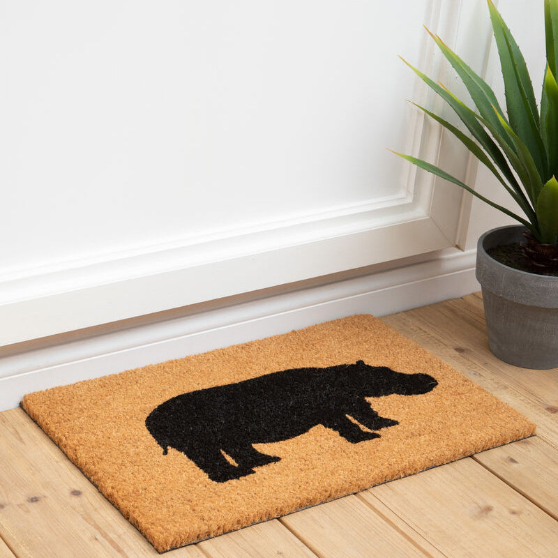 Doormat with hippo design on a wooden floor next to a plant