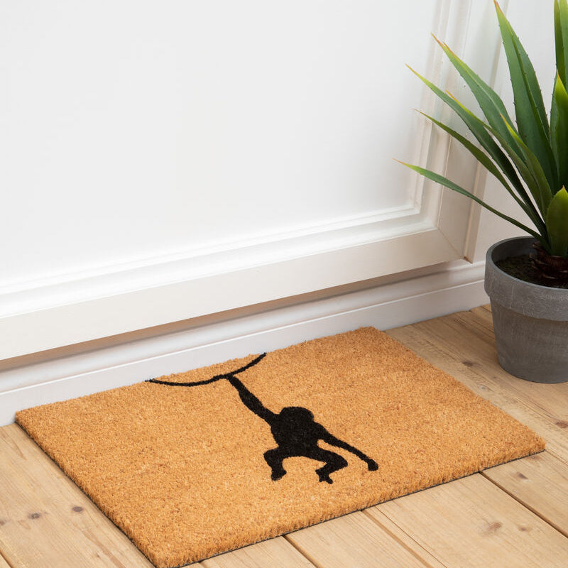 Doormat with a black silhouette design on a wooden floor next to a plant.
