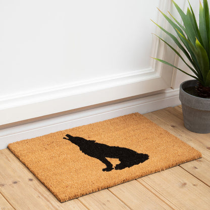 Doormat with a dog silhouette on a wooden floor next to a plant