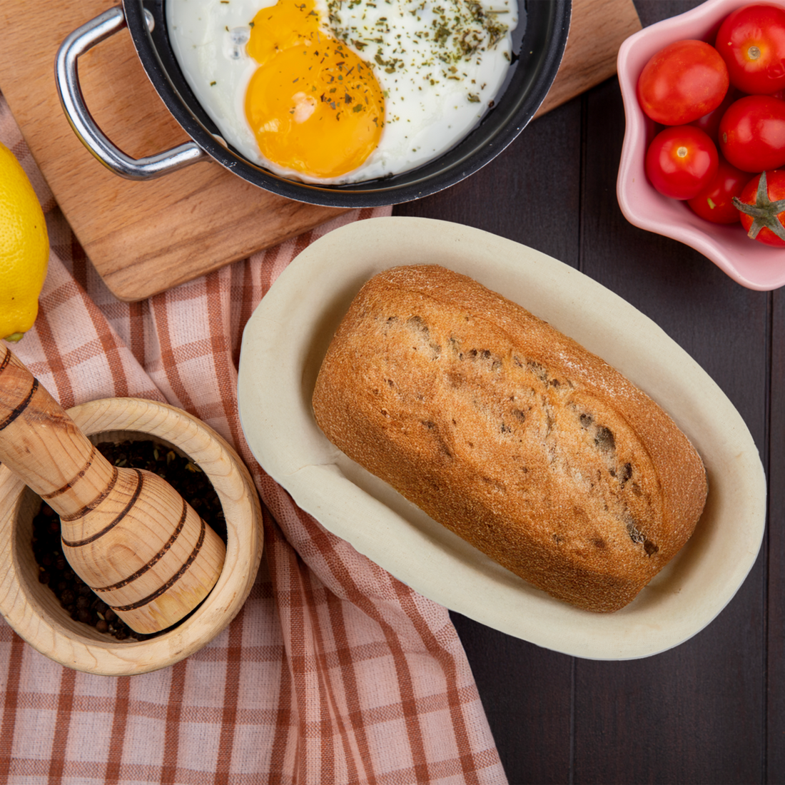 Loaf of bread on a white plate with a bowl of eggs and tomatoes in the background.