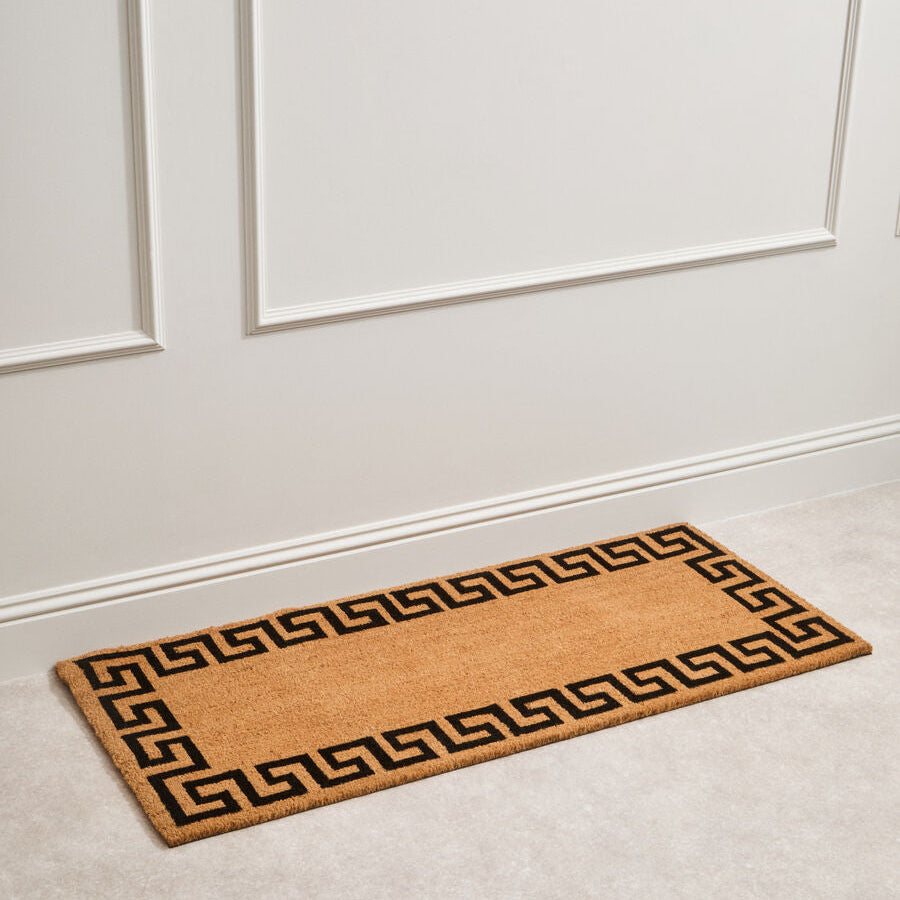 Doormat with a Greek key pattern on a white floor and wall.