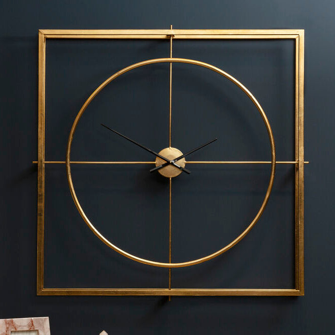 Gold wall clock on a dark wall with a lamp and decorative items on a table.