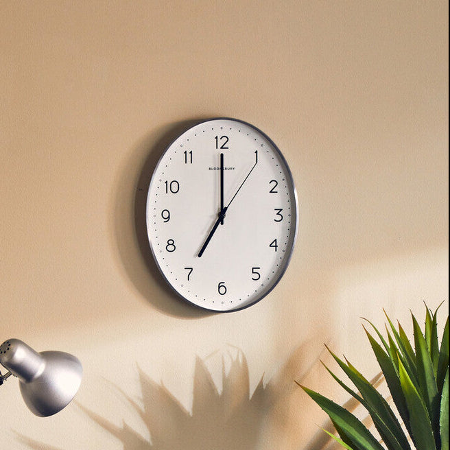 Wall clock on a beige wall above a desk with a lamp and plant.