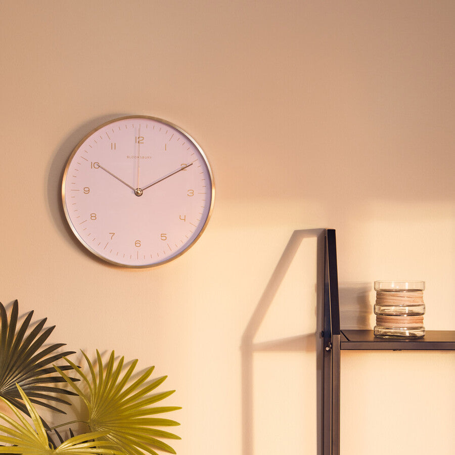 Wall clock on a beige wall with a plant and shelf in the foreground